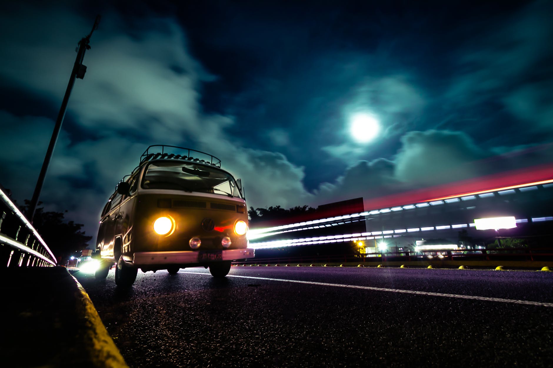 Ein VW-Bus bei Nacht auf einer Straße. Über ihm der Mond hinter Wolken.