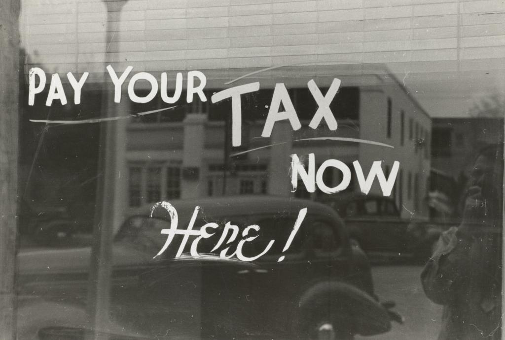 Auf einer Fensterscheibe steht der Text "Pay your tax now here!", zu deutsch "Zahl deine Steuern jetzt hier!"